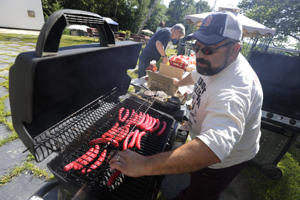 A man putting hot dogs on a BBQ. This story is about sustainable grilling tips.