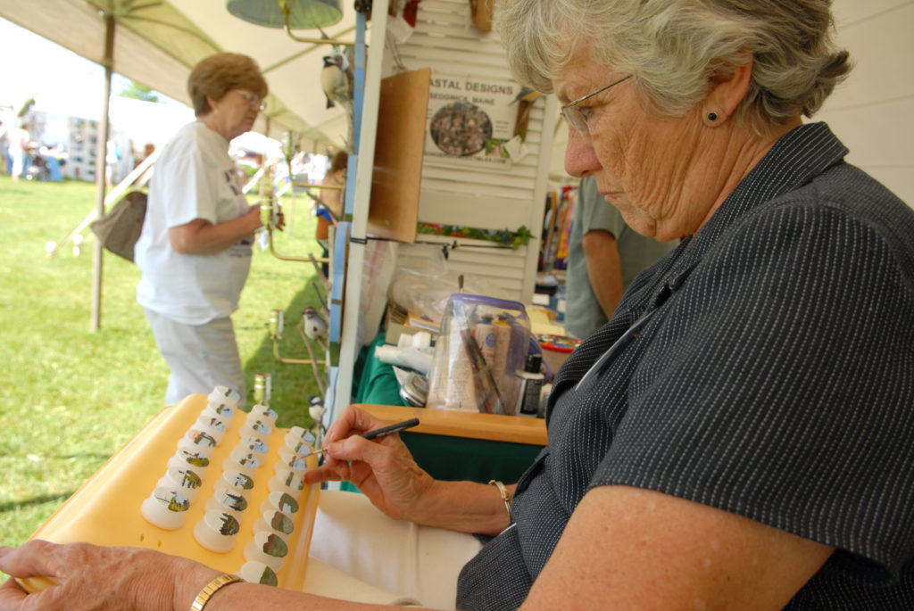 Beth Fewell, co-owner of Coastal Designs in Maine, paints miniature coastal scenes on night lights in her booth at the United Maine Craftsmen second annual Bangor Waterfront Arts & Crafts show. 