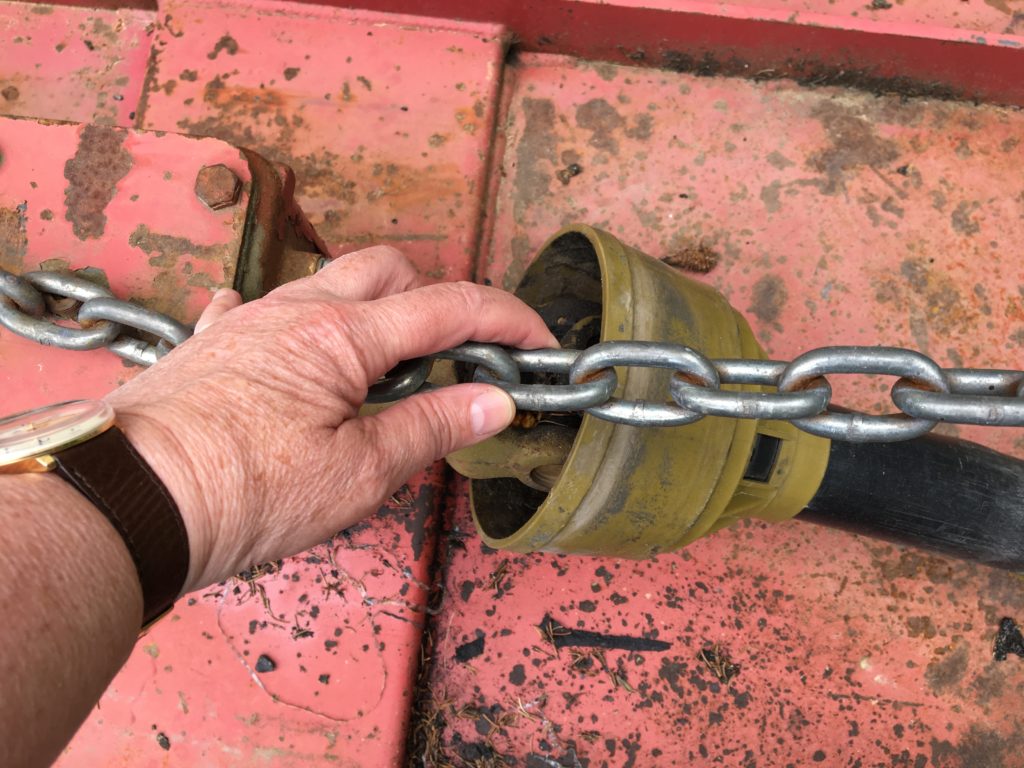 An ungloved hand grabs a chain connecting a tractor to a piece of farm machinery.