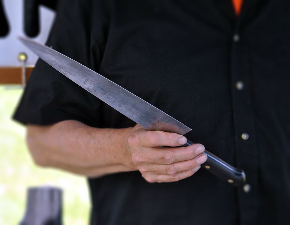 Neill Peterson, owner of ACE Sharpening and Window Cleaning in Belfast, Maine, holding a carbon steel knife.