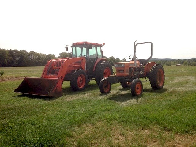 Two red tractors parked next to each other in a field. One with an enclosed cab and the other with a rollover protection system.