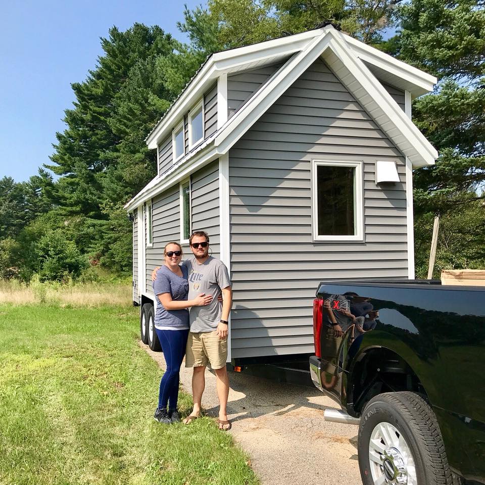 A couple stands in front of their tiny house.