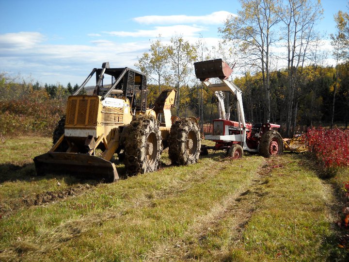 A farm tractor being pulled from the mud by a large, yellow skidder.