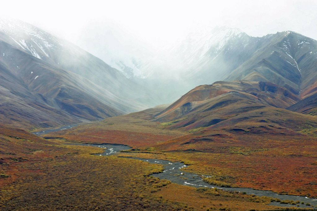 A wide shot of a tundra with a river and mountains.