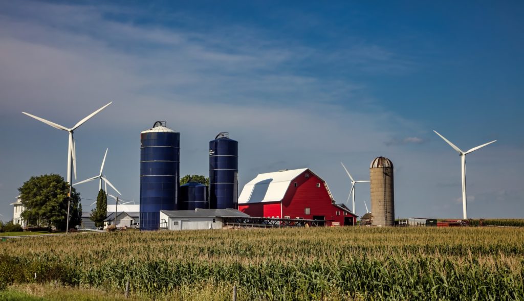 A red barn with three grain silos and four large power-generating wind turbines.