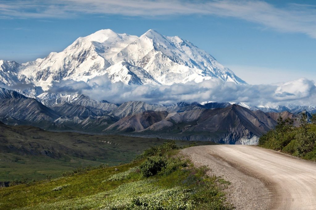 A dirt road with a tall, snow capped mountain.