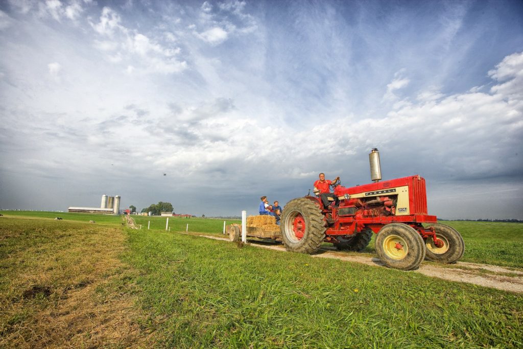 A red tractor pulling an open trailer with straw bales piled on it.