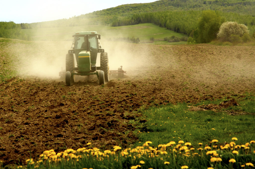 A John Deere tractor pulling tiller over a dusty field.