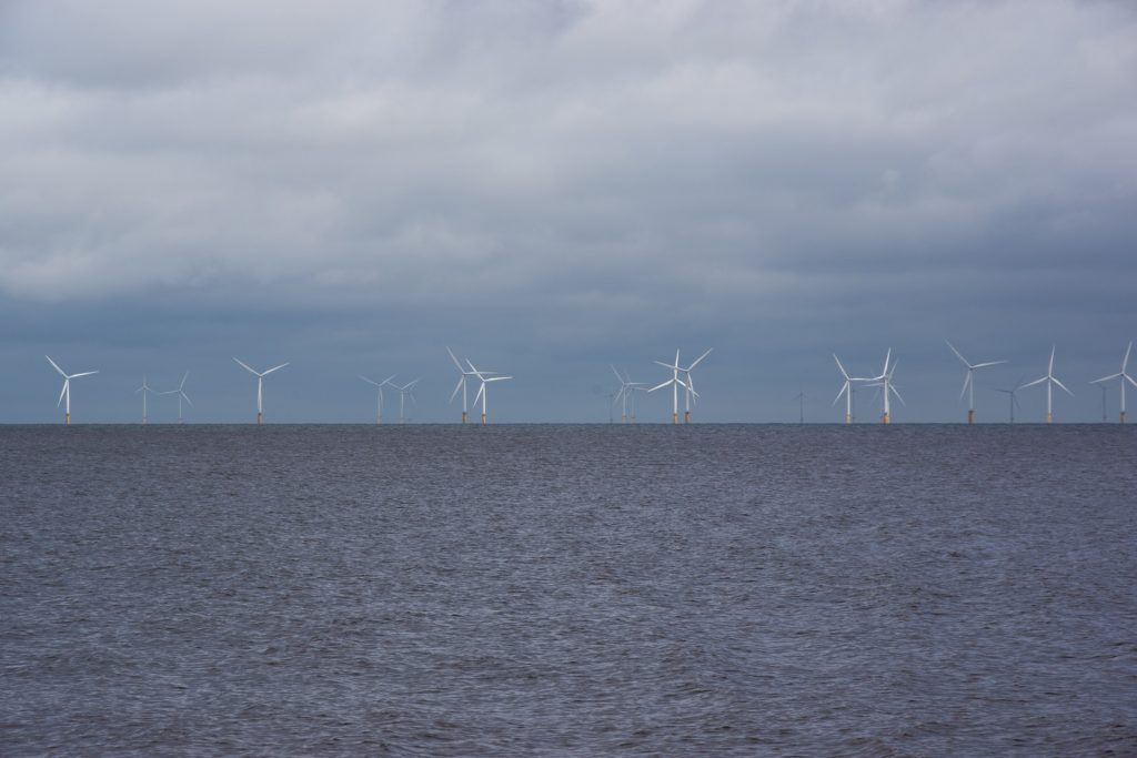 A row of large wind turbines set offshore in the ocean.